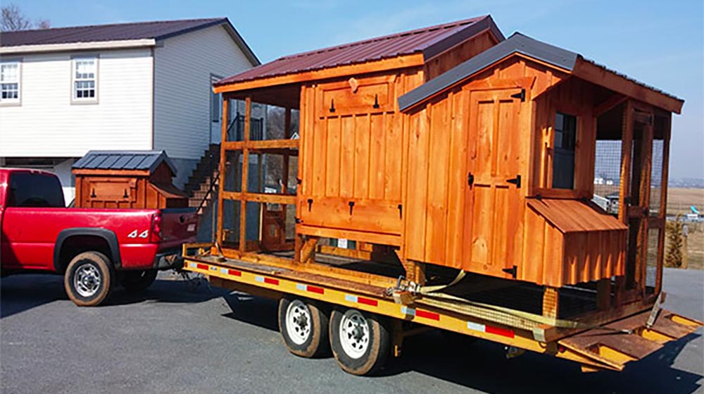 Two cedar-stained wood walk-in chicken coops on a flat-bed trailer ready to be shipped to a customer.